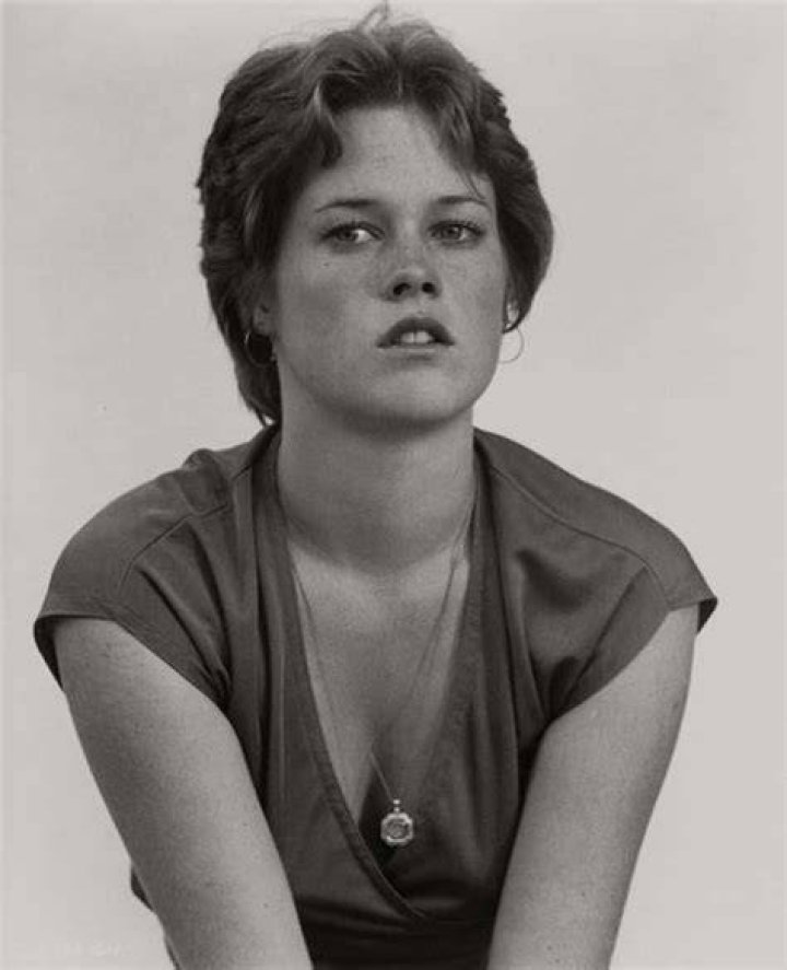 A closeup of Melanie Griffith in a white turtleneck sweater and her hair up.