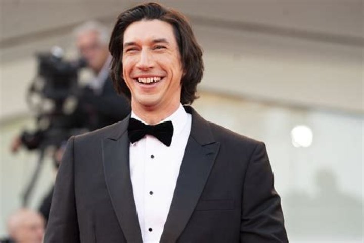 Adam Driver poses for photos in front of a purple backdrop.