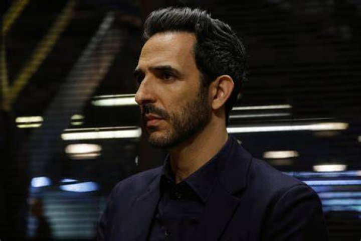 Amir Arison as Aram Mojtabai in The Blacklist Season 9. Aram kneels in front of someone wearing a blue suit.