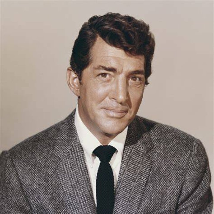 Dean Martin pokes his head and shoulder in through a locked door. Frank Sinatra stands with his arms folded and faces Martin.