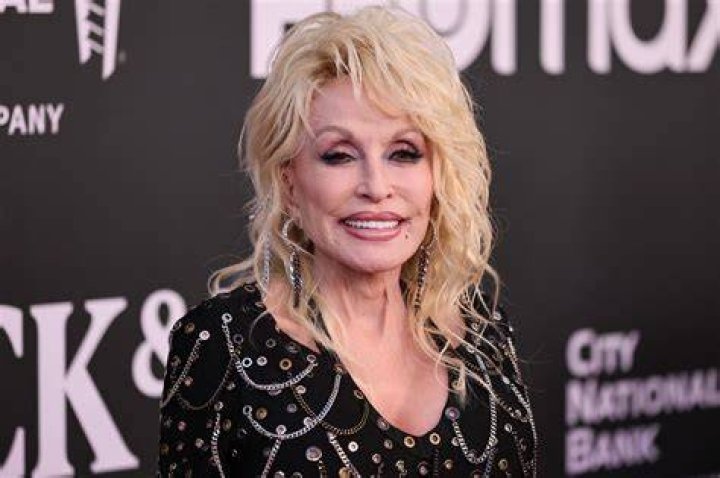Dolly Parton smiles while wearing a pink dress.