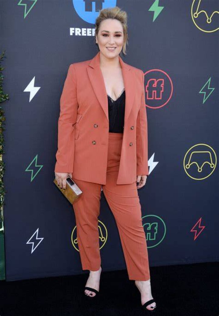 Emma Hunton smiles while wearing a peach outfit at a media event.