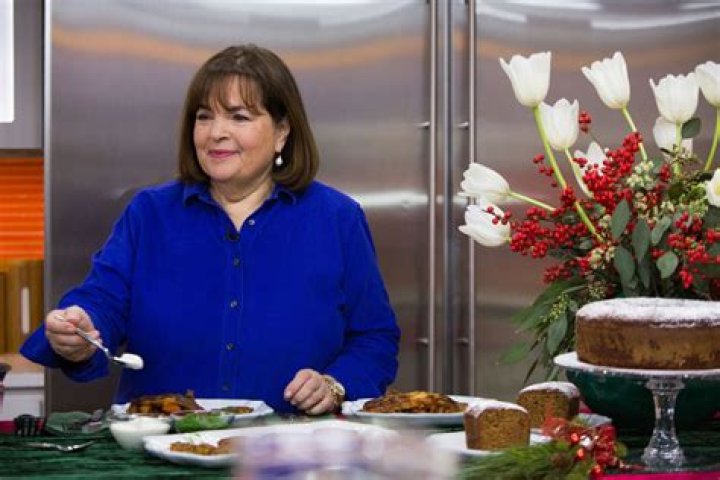 Ina Garten wears a blue shirt while smiling and toasting with a glass of wine
