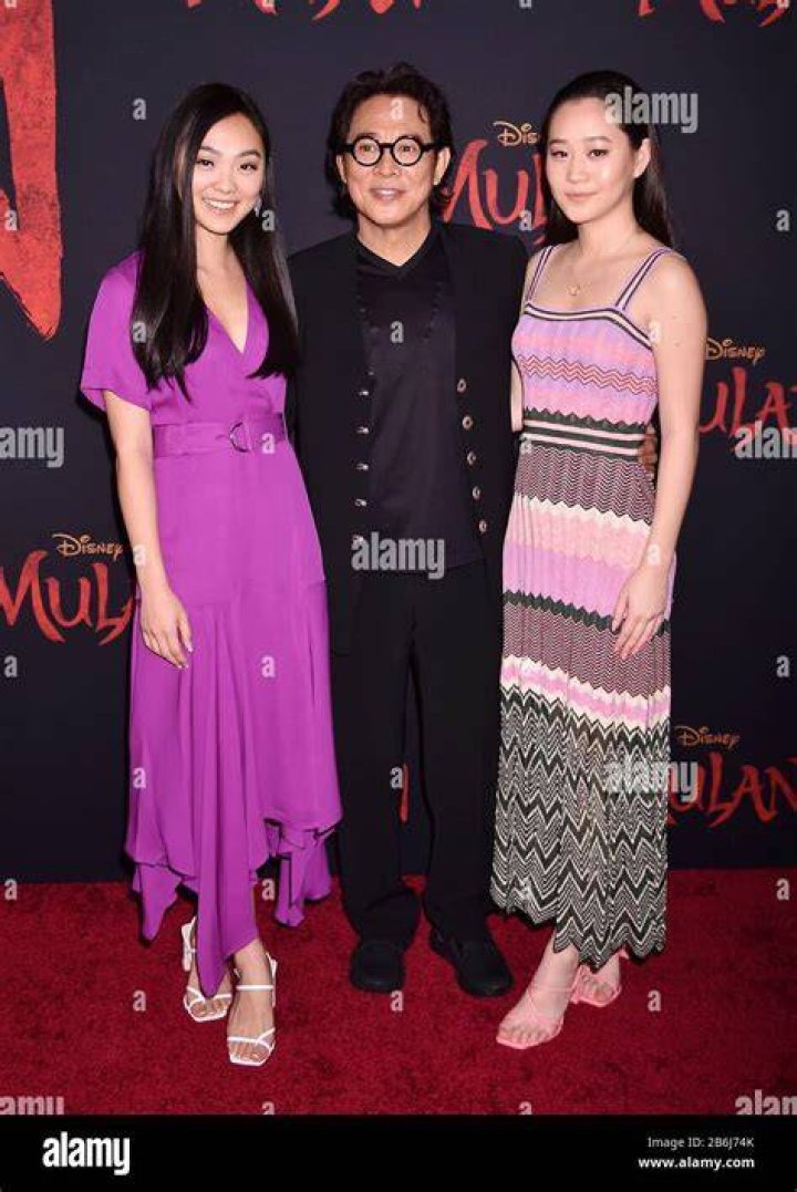 Jet Li and daughters Jane and Jada pose in front of a backdrop featuring the "Mulan" logo