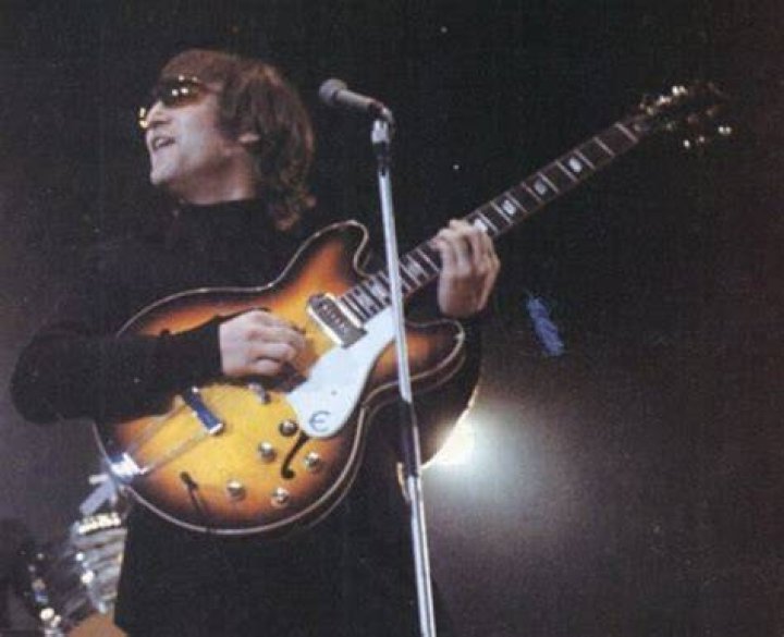 John Lennon holding a guitar while sitting