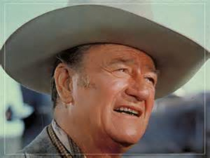 John Wayne, who had negative views on the celebration of gay rights, wearing a black-and-white tuxedo with white table-clothed tables in the background