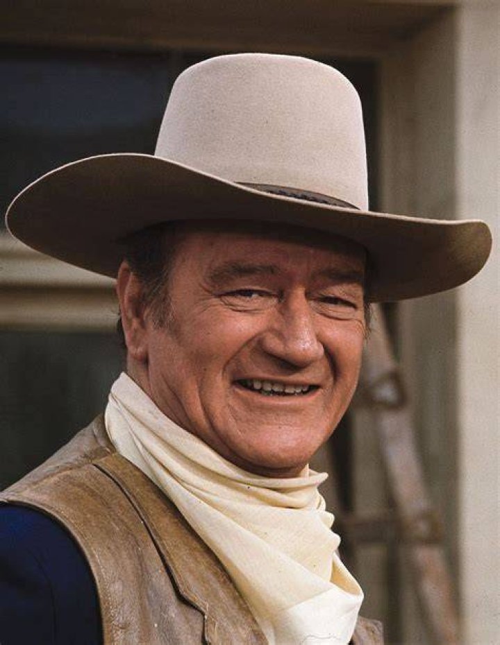 John Wayne, who submitted the John Wayne Casserole recipe, wearing a cowboy hat and holding a cigarette at an unknown dinner event
