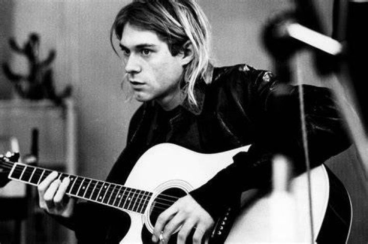 Kurt Cobain of Nirvana plays guitar and sings into the microphone.