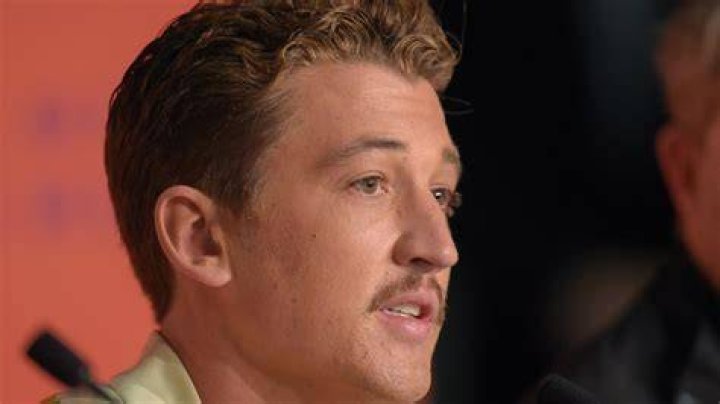 Miles Teller smirking while wearing a black suit.