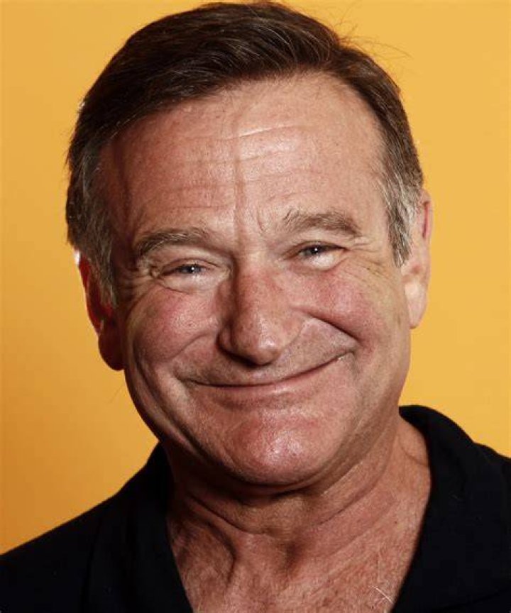 Robin Williams smiling in front of a red background